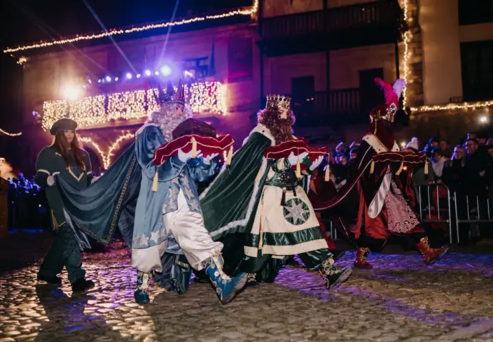Los Reyes Magos desfilan en la cabalgata de Santillana del Mar, portando regalos bajo luces festivas.