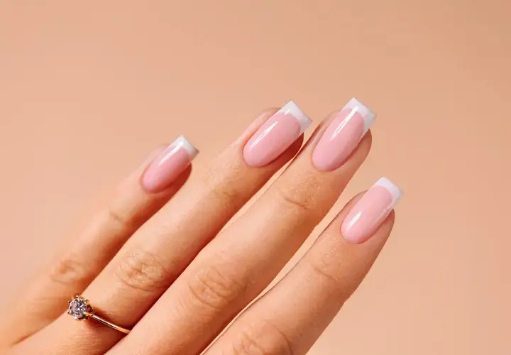 Dłoń z idealnym manicurem francuskim, ozdobiona subtelnym pierścionkiem z brylantem.