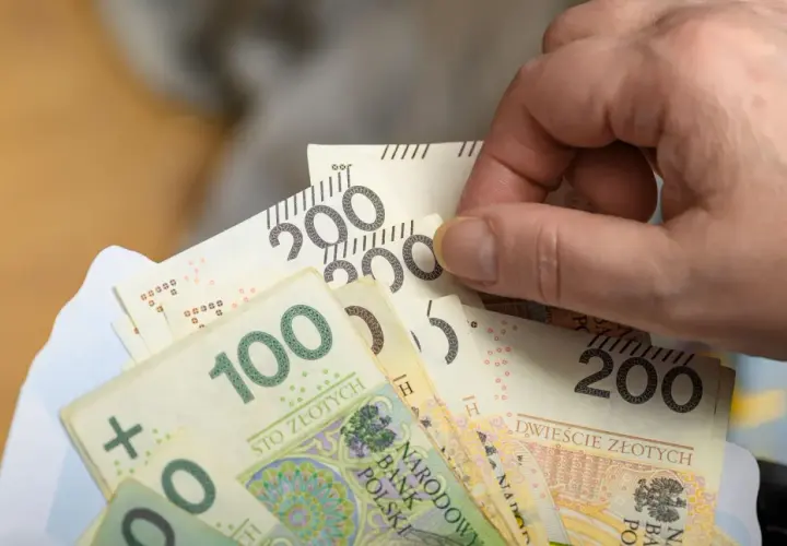 Dłoń trzyma plik banknotów 100 i 200 zł, symbolizujący nową płacę minimalną.