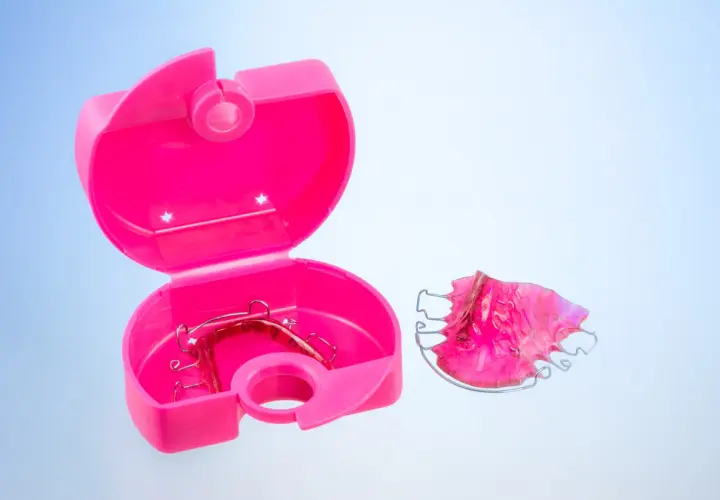 Caja ortodoncia rosa abierta con un retenedor dentro y otro fuera.