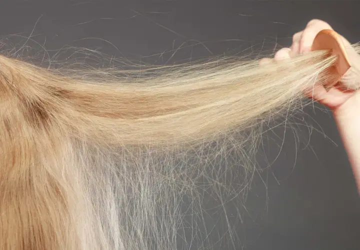 En hand håller en träkam genom blont, tunt hår. Håret ser lite slitet ut, inte krusigt.