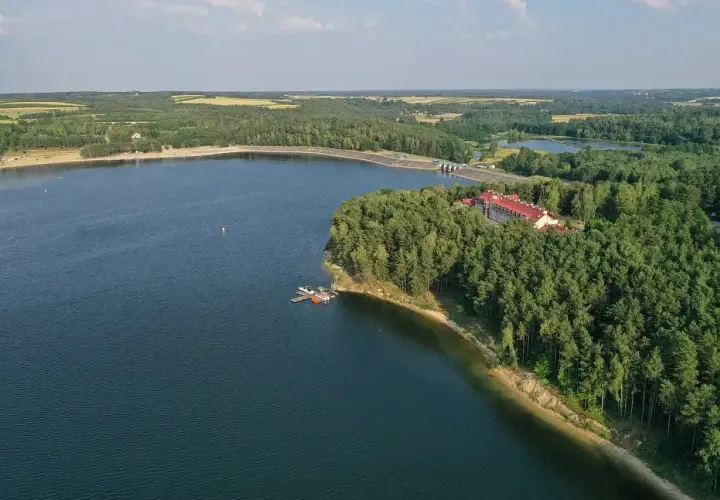 Malownicze jezioro Chańcza otoczone lasem, z hotelem i pomostem.