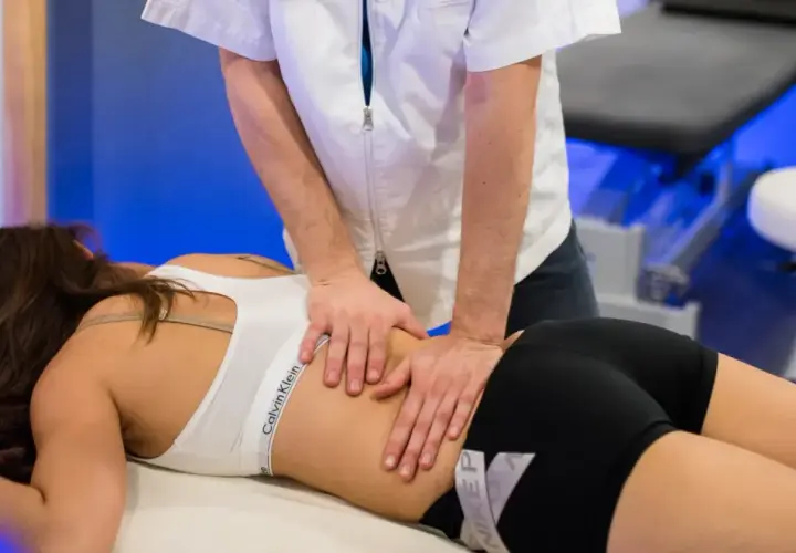 Un professionnel effectue un massage musculaire sportif sur le dos d'une femme allongée sur une table de massage.
