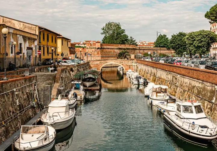 Boats docked along a canal in Livorno, Italy, with a brick bridge in the background.