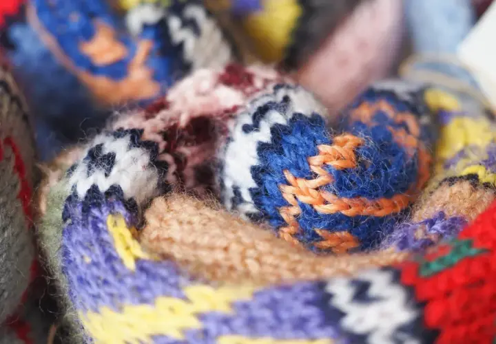 Gros plan sur un tissu jacquard aux motifs géométriques colorés, avec des fils de laine bleus, violets, jaunes et rouges entrelacés.