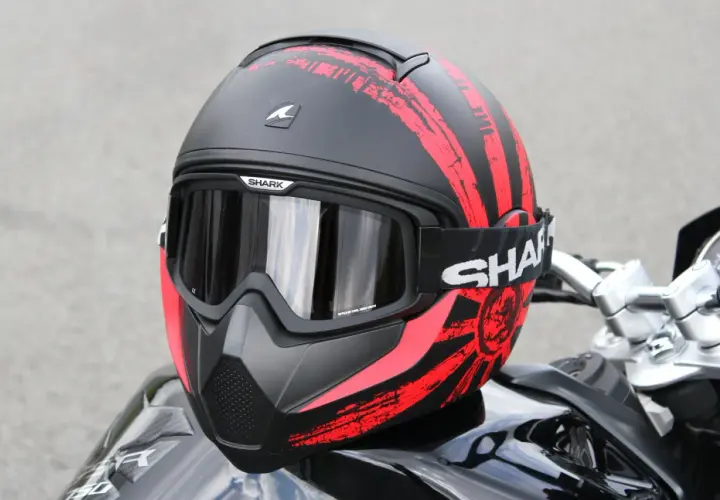 La calotta del casco Shark, nera con grafiche rosse a strisce e un sole nascente, è pronta per l'avventura.