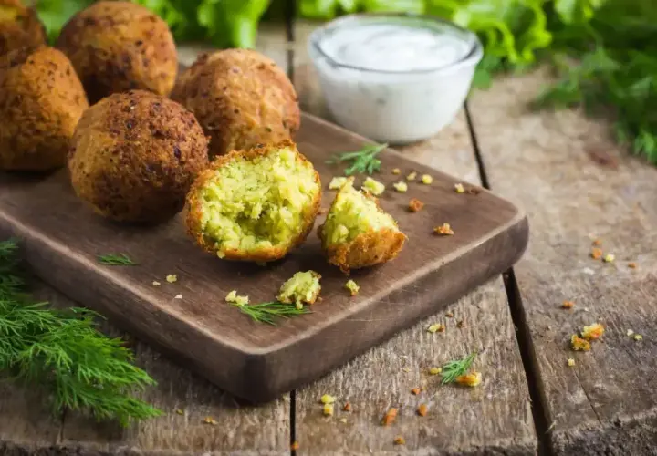 Chrupiące falafel na desce, jeden przekrojony, z sosem jogurtowym i koperkiem. Idealny falafel przepis.