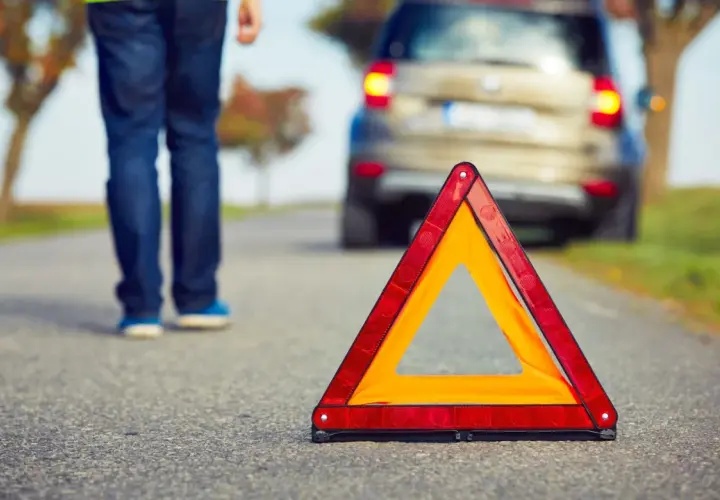 Triángulo de emergencia en carretera. Un hombre se acerca a un coche averiado, listo para proteger, avisar y socorrer.