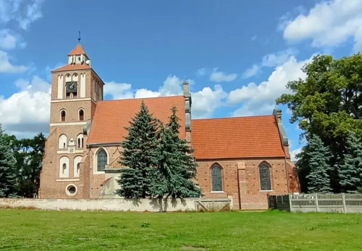 Nieszawa atrakcje: ceglany kościół z wieżą i zegarem, otoczony zielenią, pod błękitnym niebem z chmurami.