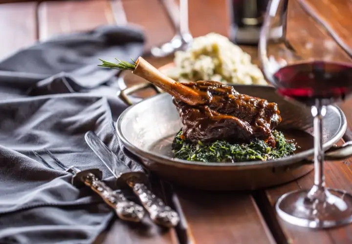 Un plat de vin avec agneau, servi sur un lit d'épinards, avec une branche de romarin. Un verre de vin rouge est à côté.