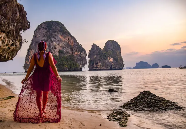 Kobieta w zwiewnej sukience spaceruje po plaży Ao Nang, podziwiając skaliste wysepki o zachodzie słońca.