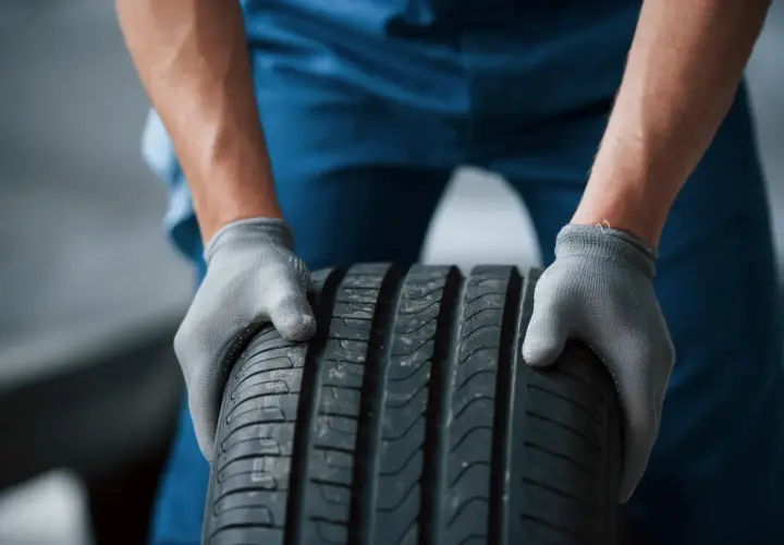 Mechanik w szarych rękawiczkach trzyma oponę radialną.