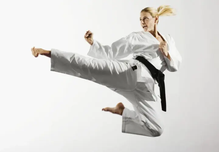 Kobieta w białym karate gi wykonuje wysokie kopnięcie w powietrzu.