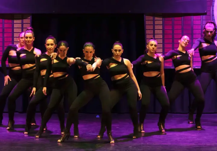 Un gruppo di ballerine in abiti neri si esibisce su un palco illuminato, creando un'atmosfera da dance hall.