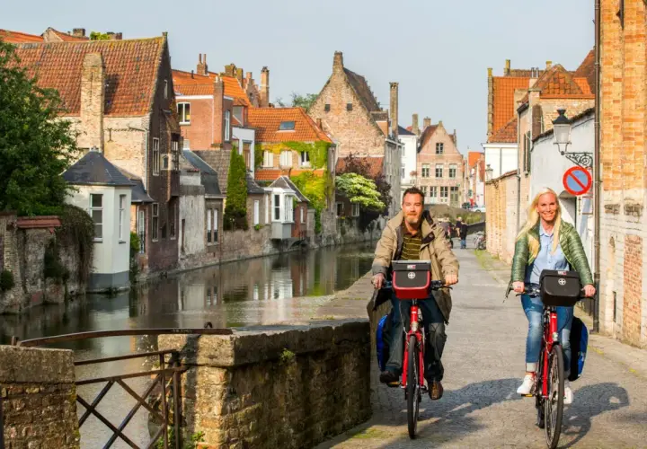 Couple enjoying a Bruges bike tour along a canal, with historic buildings lining the waterway.