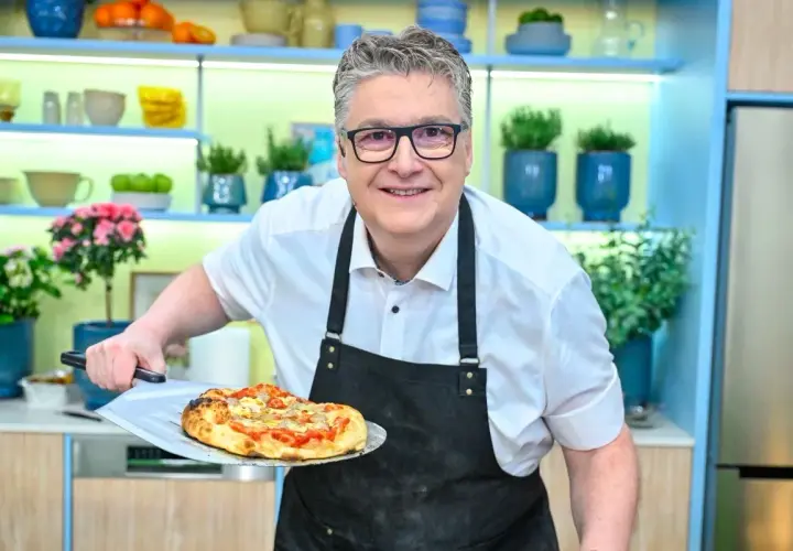 Uśmiechnięty kucharz prezentuje pyszną pizzę rzymską prosto z pieca.