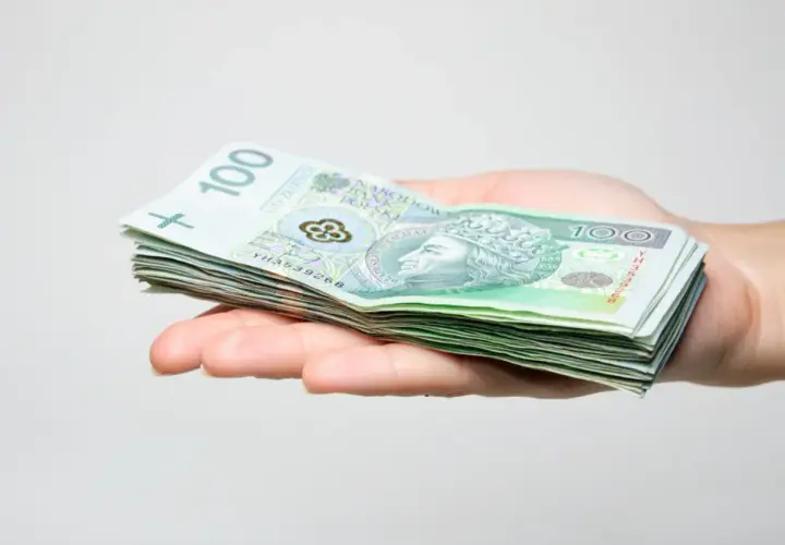 Dłoń trzyma stos banknotów 100 zł. Jak wypełnić wniosek SD-Z2?