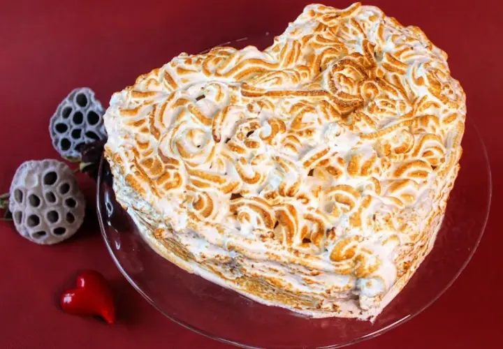 Serce z bezy, pyszne ciasto bez cholesterolu, ozdobione wzorami. Obok suszone kwiaty i czerwone serduszko.