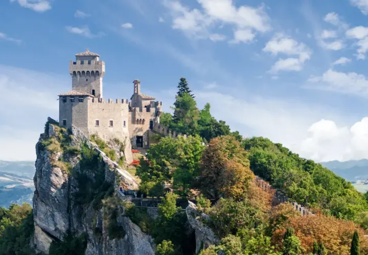 Trzy wieże San Marino na skalistym szczycie, otoczone zielenią. Widok na doliny, gdzie mieszka san marino ludność.