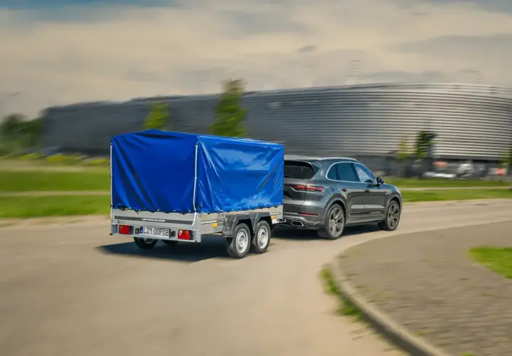 Szary SUV ciągnie dwuosiową przyczepę pod niebieską plandeką. Czy można ciągnąć przyczepę dwuosiową na kat. B?