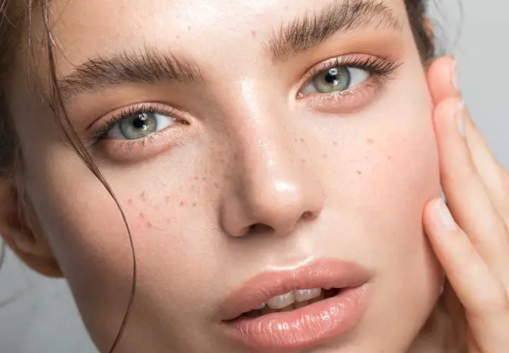 Un visage de femme aux yeux verts et aux taches de rousseur. La poudre libre matifie et fixe le maquillage pour un teint parfait.
