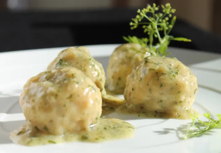 Quattro polpette in umido, ricoperte da una salsa cremosa alle erbe, servite su un piatto bianco con guarnizione di prezzemolo.