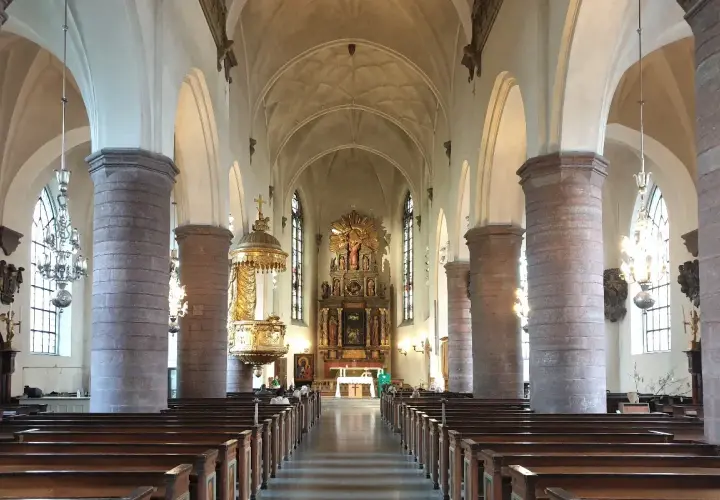 Interiör av St Jacobs kyrka med bänkar, pelare och altare.