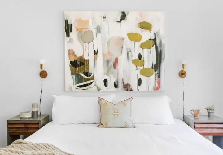 Staging a master bedroom with a large abstract painting above a white bed, flanked by modern nightstands and sconces.