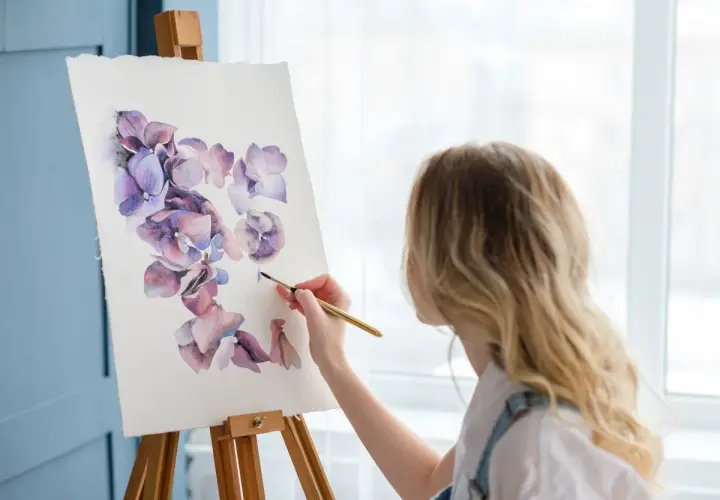 Kobieta maluje akwarelami fioletowe kwiaty. To inspiracja, jak być kreatywnym, tworząc piękno.