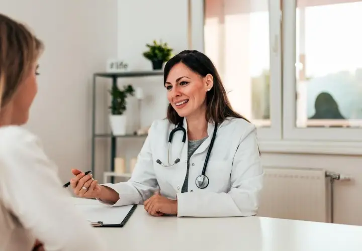 Medico sorridente parla con paziente, illustrando un punto con la penna. La scena evidenzia una buona comunicazione medico-paziente.