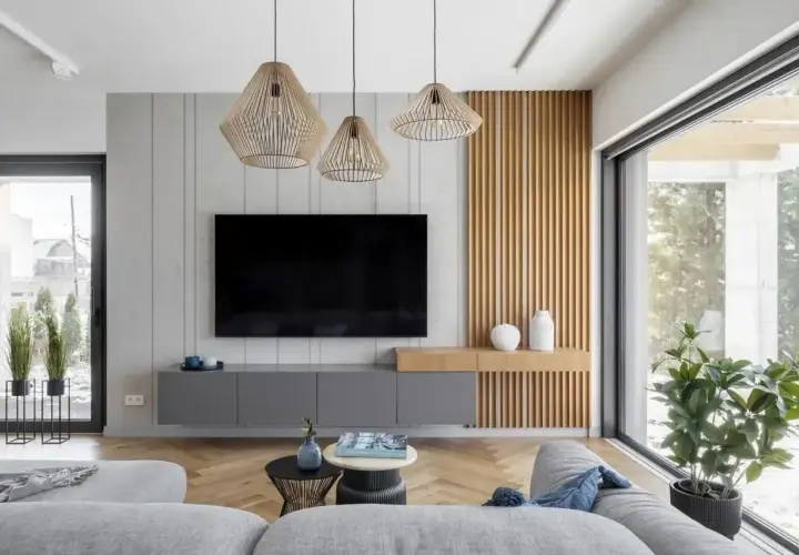 Nowoczesny salon z szarymi meblami i drewnianymi panelami. Trzy wiszące lampy tworzą przytulną atmosferę, idealną do relaksu. Zastanawiasz się, ile lumenów do salonu?
