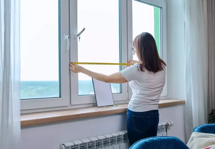 Une femme mesure une fenêtre, pensant à l'avantage d'un achat immobilier neuf pour personnaliser son espace.