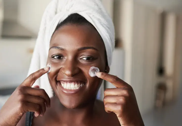 Sonrisa radiante de mujer con toalla en la cabeza, aplicándose crema. Un vistazo al **retinol antes y después** para una piel luminosa.