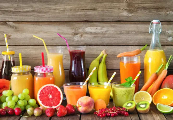 Varietà di bevande colorate e freschi estratti di frutta, con frutta intera e a fette su uno sfondo di legno.