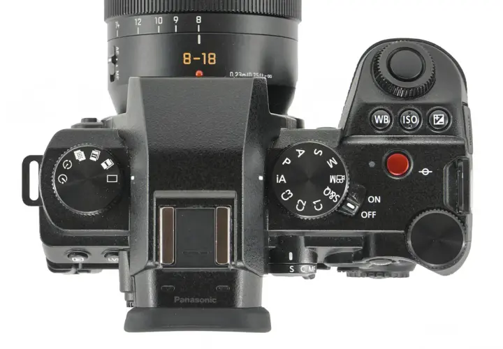 Górna część aparatu Panasonic Lumix G9 II z obiektywem 8-18 mm. Widoczne pokrętła trybów, przyciski i ekran.