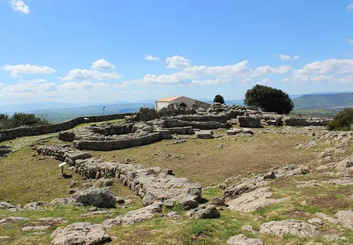 Rovine del santuario nuragico di Santa Vittoria sotto un cielo azzurro con nuvole bianche.