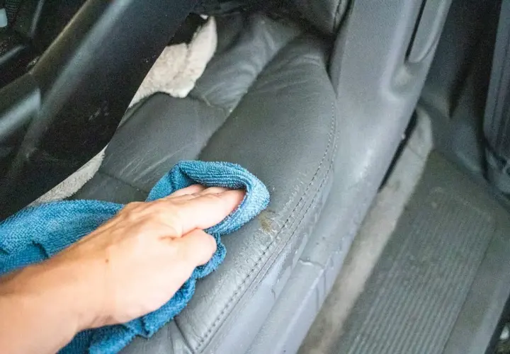 Ręka z niebieską ściereczką czyści skórzane fotele samochodowe.