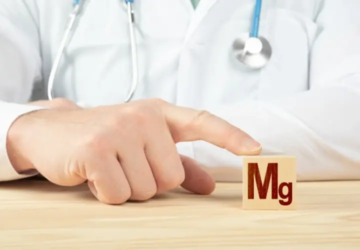 Lekarz w białym kitlu wskazuje palcem na kostkę z napisem "Mg".
