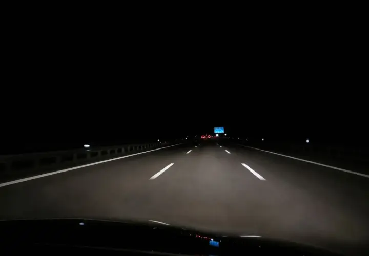 Fahrt über die Autobahn nachts. Scheinwerfer beleuchten die Fahrbahn, weiße Linien weisen den Weg in die Dunkelheit.