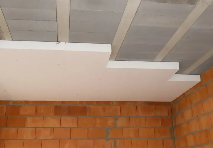 Ocieplenie stropu styropianem w trakcie budowy. Widoczne ceglane ściany i betonowy strop z elementami izolacji.