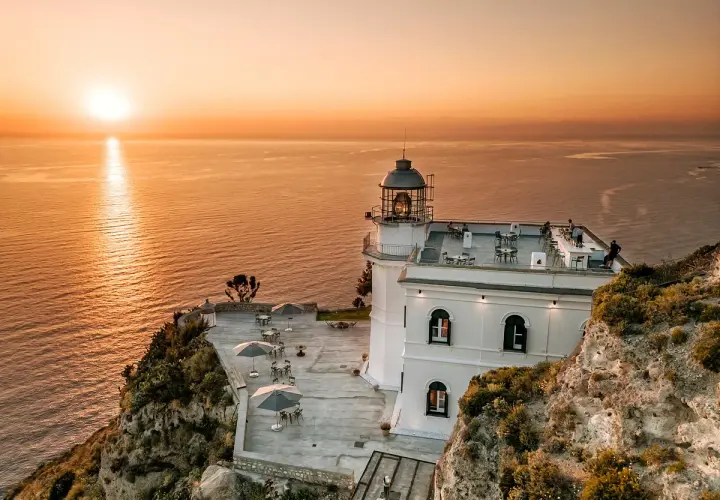 Hotel Faro Punta Imperatore a Ischia, con il sole che tramonta sul mare. Tavolini all'aperto e un bar sul tetto.