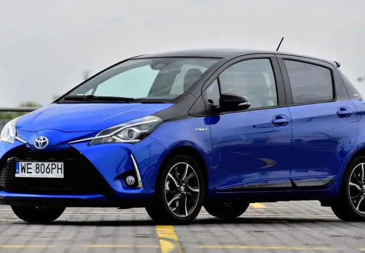Niebieska Toyota Yaris Hybrid, z czarnym dachem, zaparkowana na zewnątrz. Ile koni ma Toyota Yaris? Ten model ma 100 KM.