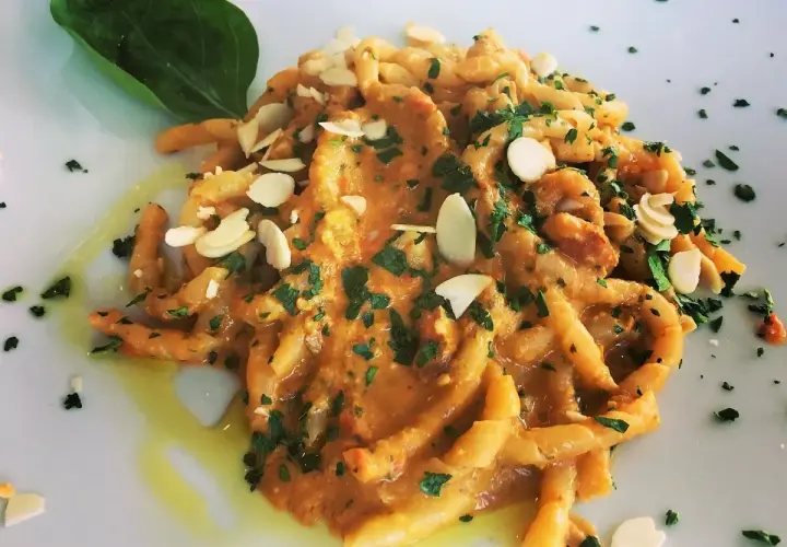 Busiate alla trapanese, un piatto di pasta siciliana con un sugo ricco, guarnito con mandorle a lamelle e prezzemolo fresco.