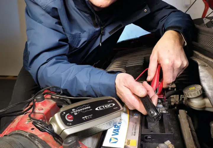 Mężczyzna podłącza prostownik CTEK do akumulatora, by sprawdzić, jak sprawdzić czy prostownik jest dobry.