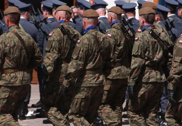 Żołnierze w mundurach polowych maszerują w szyku, każdy z bagnetem na karabinie.