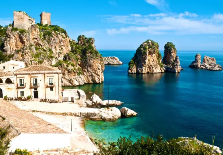 Torri e case antiche su scogliere rocciose, con faraglioni nel mare blu. Un paesaggio che evoca la storia dei bizantini in Sicilia.