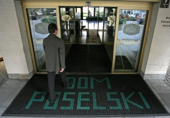 Mężczyzna wchodzi do hotelu poselskiego. Na wycieraczce przed wejściem widnieje napis "DOM POSELŚKI".