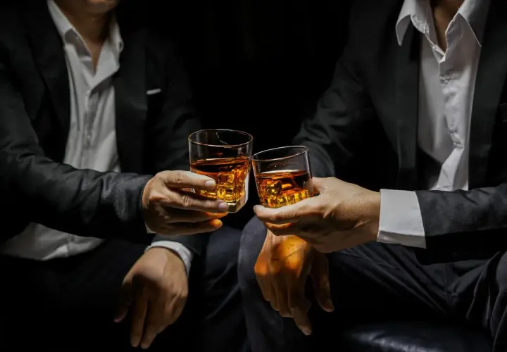 Deux hommes en costume portent des verres de whisky ambré, évoquant la définition d'un single malt : pur, authentique, une expérience unique.