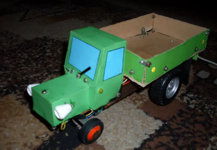 Zielony traktor z kartonu, z niebieskimi szybami i drewnianą skrzynią. Oto jak zrobić taki traktor z kartonu!