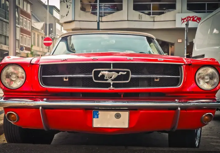 Czerwony Ford Mustang z lat 60. z emblematem galopującego konia na grillu.